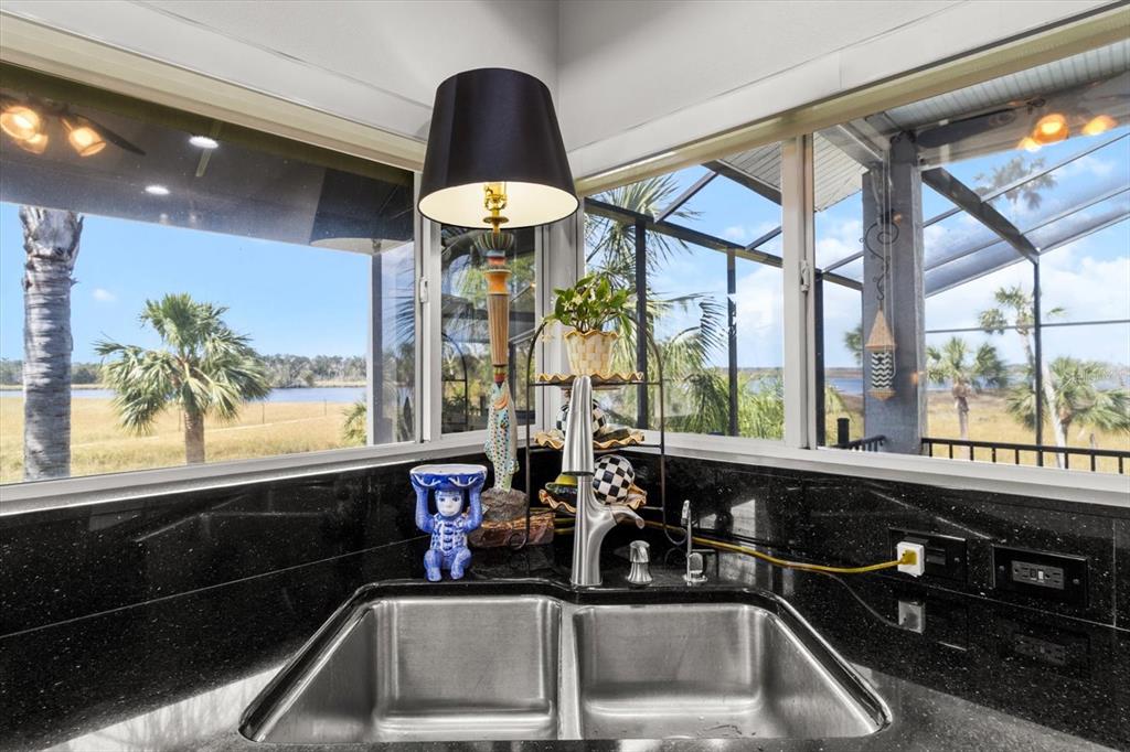 A kitchen sink with black granite countertops overlooks a view of palm trees and water — 11927 W TIMBERLANE DRIVE, HOMOSASSA, FL