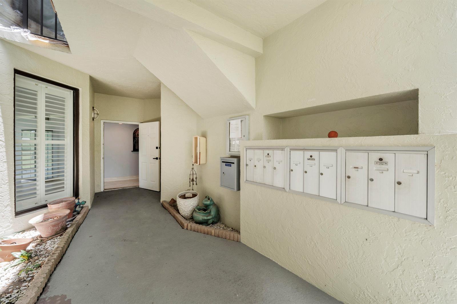An outdoor entryway features a row of metal mailboxes, potted plants, and a doorway — 6371 La Costa Drive # 104, Boca Raton FL 33433, BOCA RATON, FL