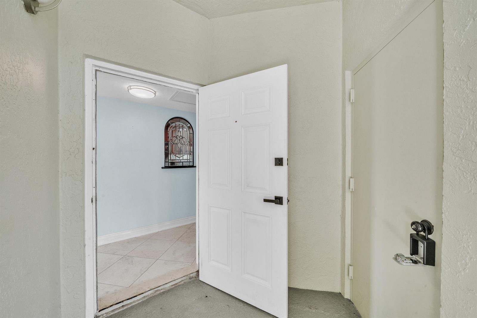 An open white door reveals a tiled entryway with a decorative arched window inside — 6371 La Costa Drive # 104, Boca Raton FL 33433, BOCA RATON, FL