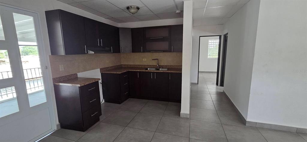 A kitchen features dark brown cabinets, granite countertops, and light-colored tile flooring — Calle 15 C-3 SAN FERNANDO, BAYAMON, PR