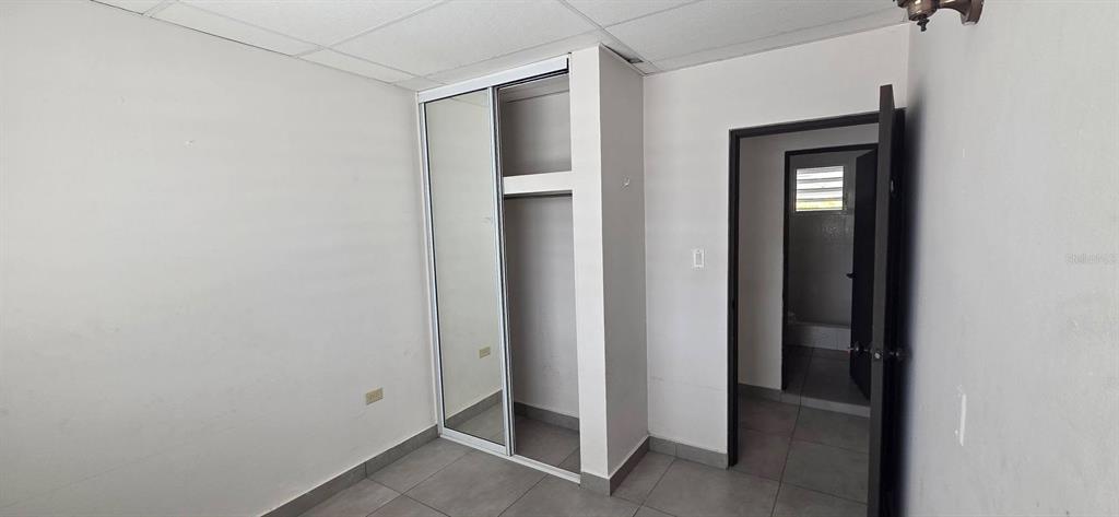 A bedroom with white walls, tiled flooring, a mirrored closet, and an open doorway — Calle 15 C-3 SAN FERNANDO, BAYAMON, PR