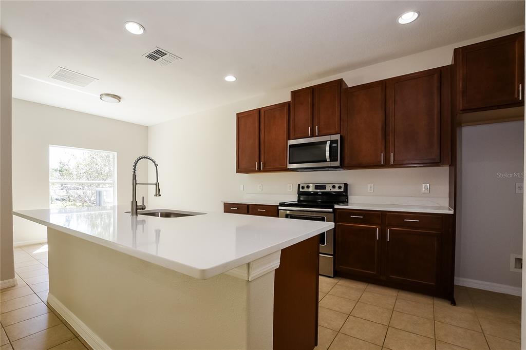 A kitchen features dark wood cabinets, white countertops, a center island, and stainless steel appliances — 12104 CITRUSWOOD DRIVE, ORLANDO, FL