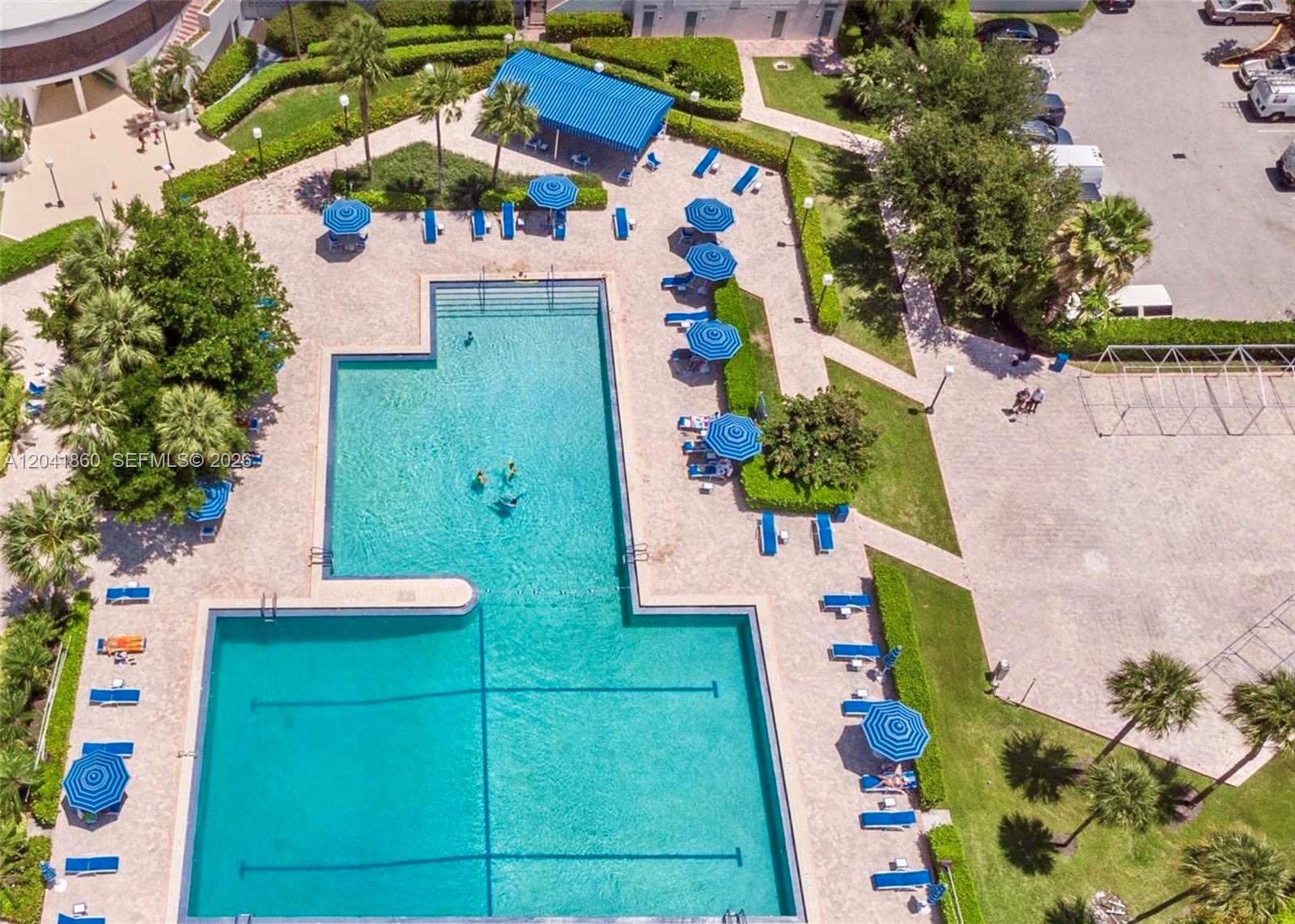An aerial view shows a large swimming pool with blue umbrellas and lounge chairs — 500 Three Islands Blvd # 223, Hallandale Beach FL 33009, HALLANDALE BEACH, FL