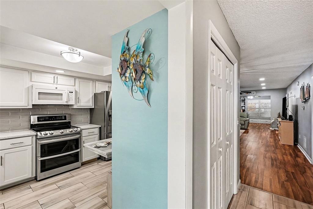 A kitchen with white cabinets and stainless steel appliances opens to a wood-floored living area — 1659 S LAKE AVENUE UNIT 1, CLEARWATER, FL