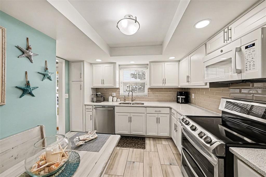 A kitchen features white cabinets, stainless steel appliances, a light-colored backsplash, and a dining area — 1659 S LAKE AVENUE UNIT 1, CLEARWATER, FL
