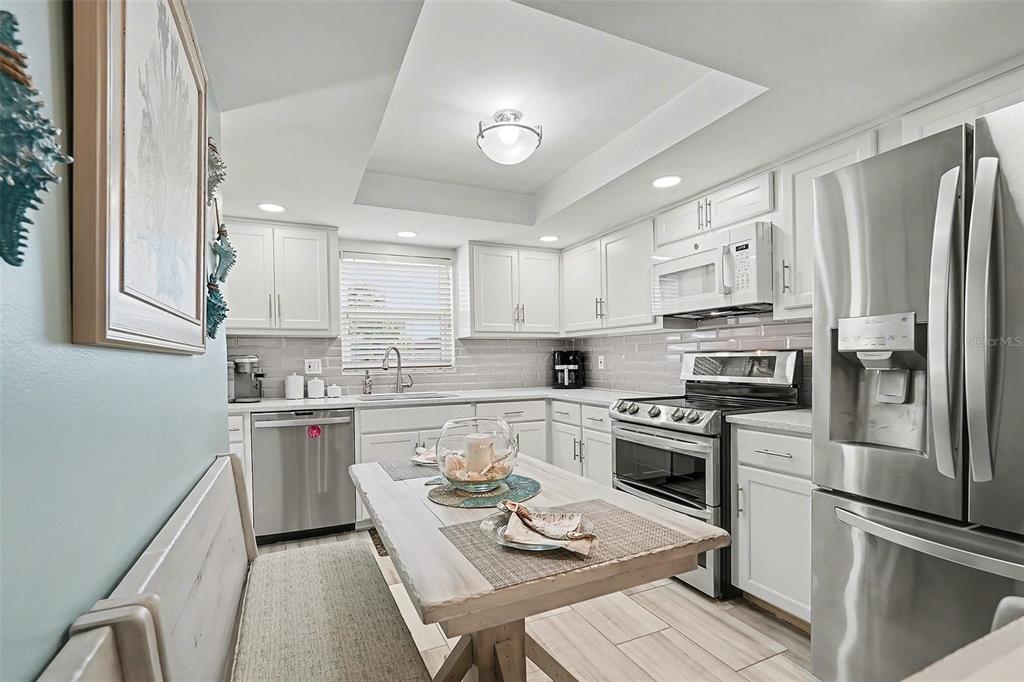 A kitchen features white cabinets, stainless steel appliances, a gray tile backsplash, and a dining table — 1659 S LAKE AVENUE UNIT 1, CLEARWATER, FL