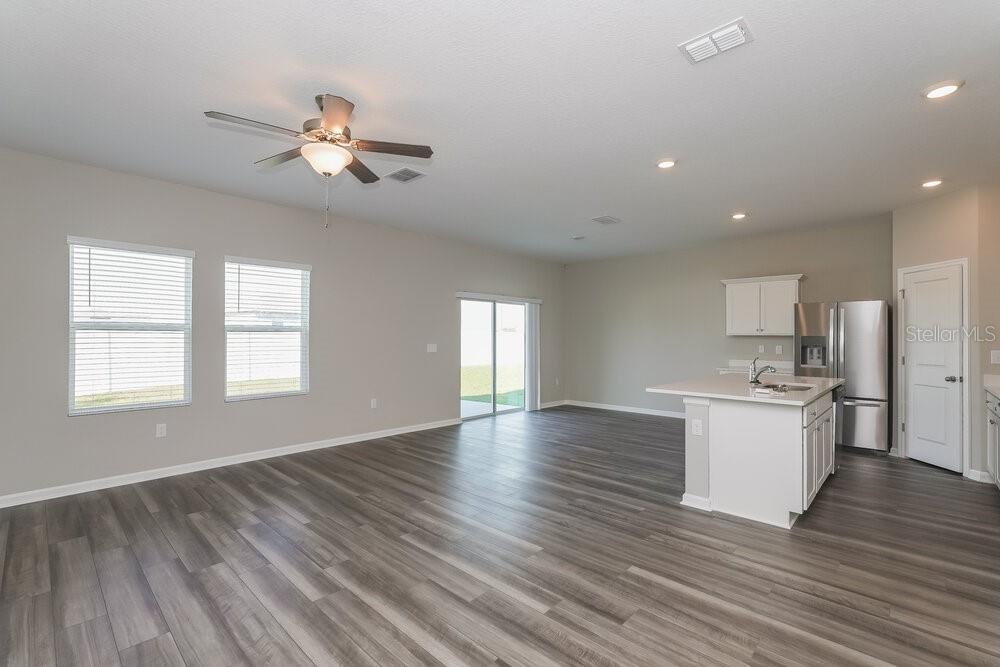 An open-concept living area with gray wood-look flooring, a kitchen island, and sliding glass doors — 954 KELLY FERN LOOP, RUSKIN, FL