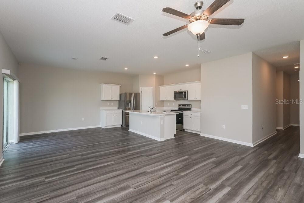 An open-concept kitchen and living area featuring white cabinetry, a center island, and wood-look flooring — 954 KELLY FERN LOOP, RUSKIN, FL