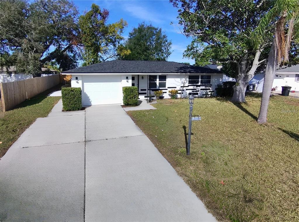 A single-story white house with a black roof, a concrete driveway, and a front lawn — 7521 BOUGENVILLE DRIVE, PORT RICHEY, FL