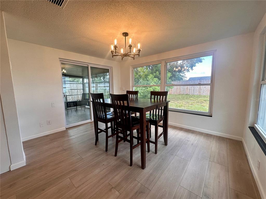 A dining room with wood-look flooring, a dark wood table set, and large windows — 7521 BOUGENVILLE DRIVE, PORT RICHEY, FL