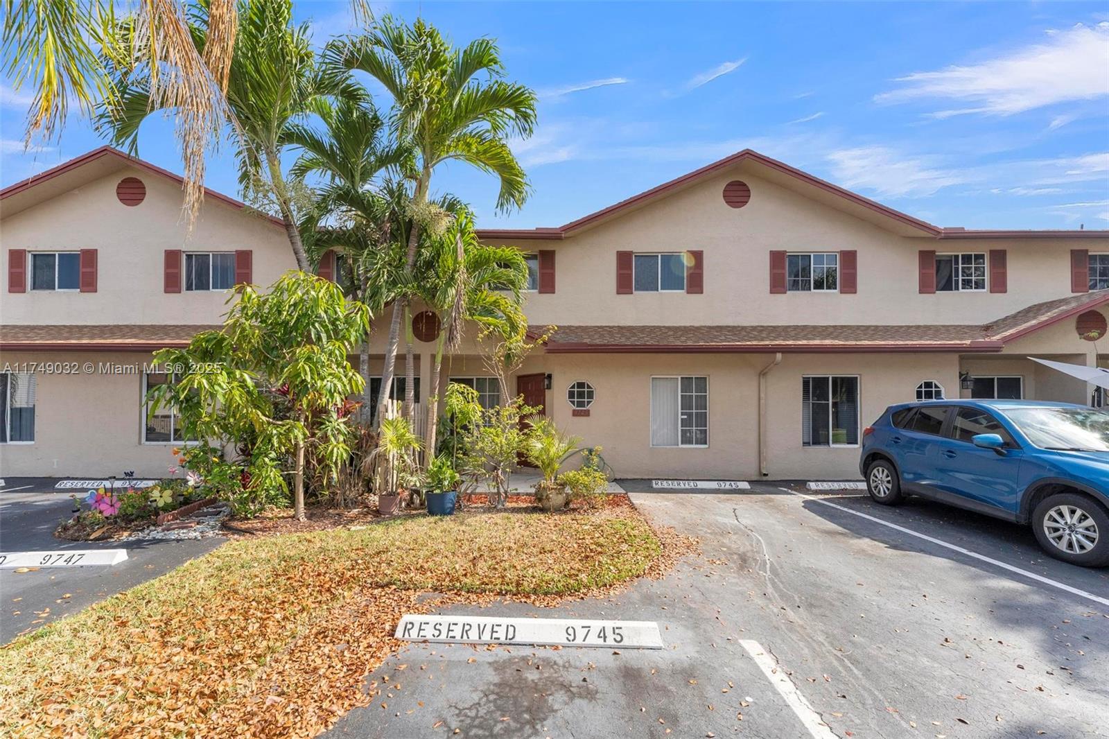 A two-story townhouse exterior features tan stucco walls, brown trim, and reserved parking spaces — 9745 NW 37th St # 9745, Sunrise FL 33351, SUNRISE, FL