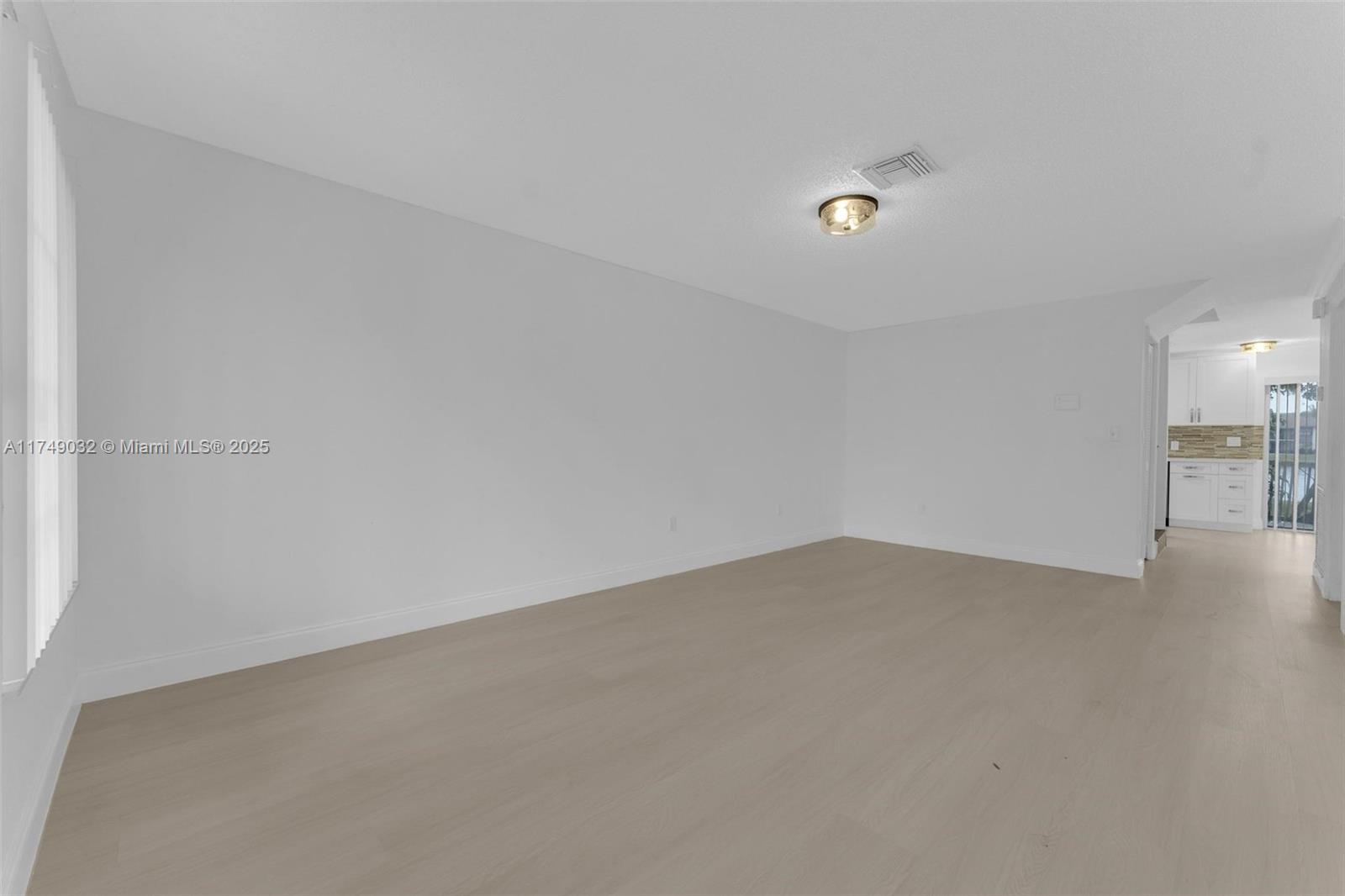 An empty room with light wood-look flooring and white walls leads to a kitchen — 9745 NW 37th St # 9745, Sunrise FL 33351, SUNRISE, FL