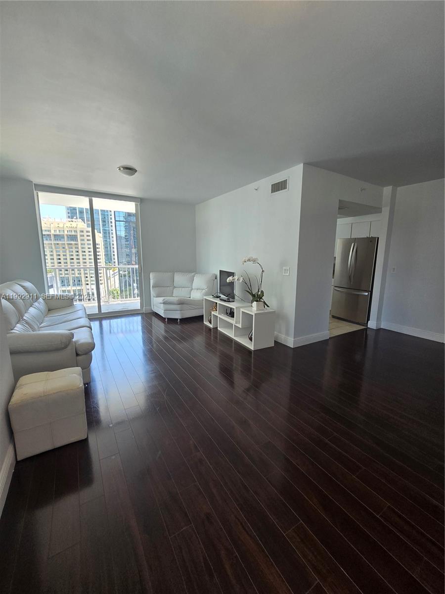 A living room with dark hardwood floors, white furniture, and a view of city buildings — 1250 S Miami Ave # 1514, Miami FL 33130, MIAMI, FL