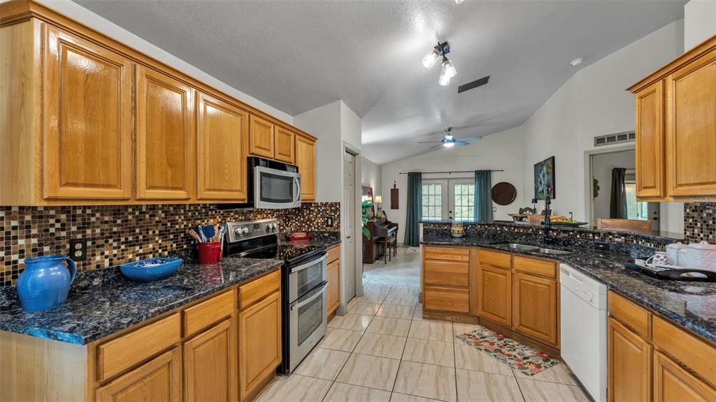 A kitchen with oak cabinets, dark granite countertops, and a mosaic tile backsplash — 13409 SWEET HILL ROAD, POLK CITY, FL