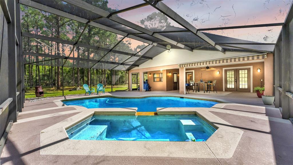 A screened-in pool and spa area with a covered patio and wooded backyard view — 13409 SWEET HILL ROAD, POLK CITY, FL