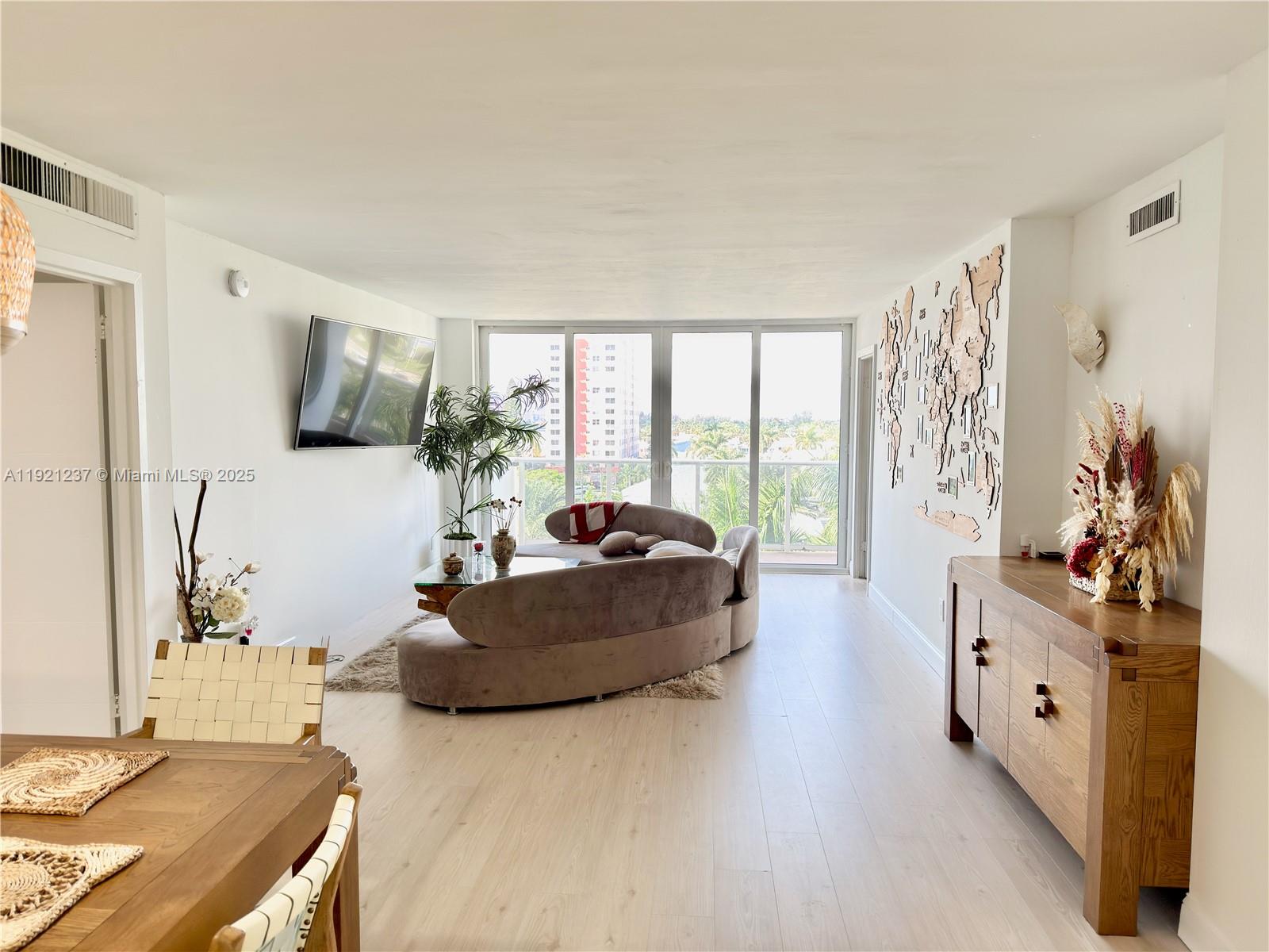 A living room features light wood flooring, a curved sofa, and a wall-mounted world map — 3140 S Ocean Dr # 512, Hallandale Beach FL 33009, HALLANDALE BEACH, FL