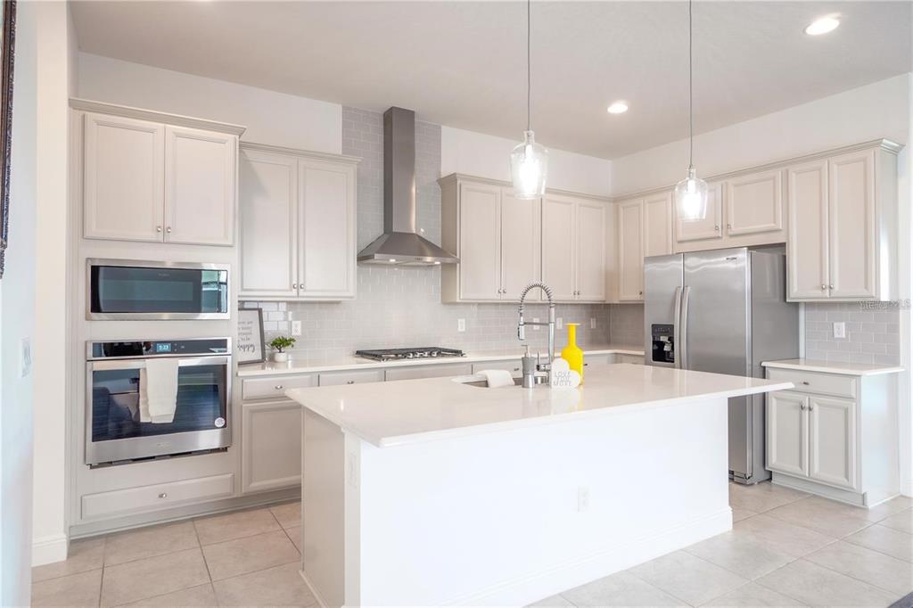 A modern kitchen features light-colored cabinetry, stainless steel appliances, a center island, and tile flooring — 15701 VETTA DRIVE, MONTVERDE, FL