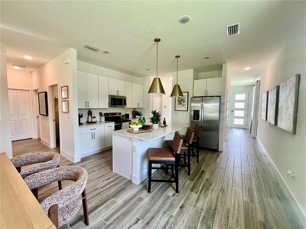 A modern kitchen features white cabinetry, a central island with bar seating, and wood-look flooring — 280 ELENA LAVIN CIRCLE, ORLANDO, FL