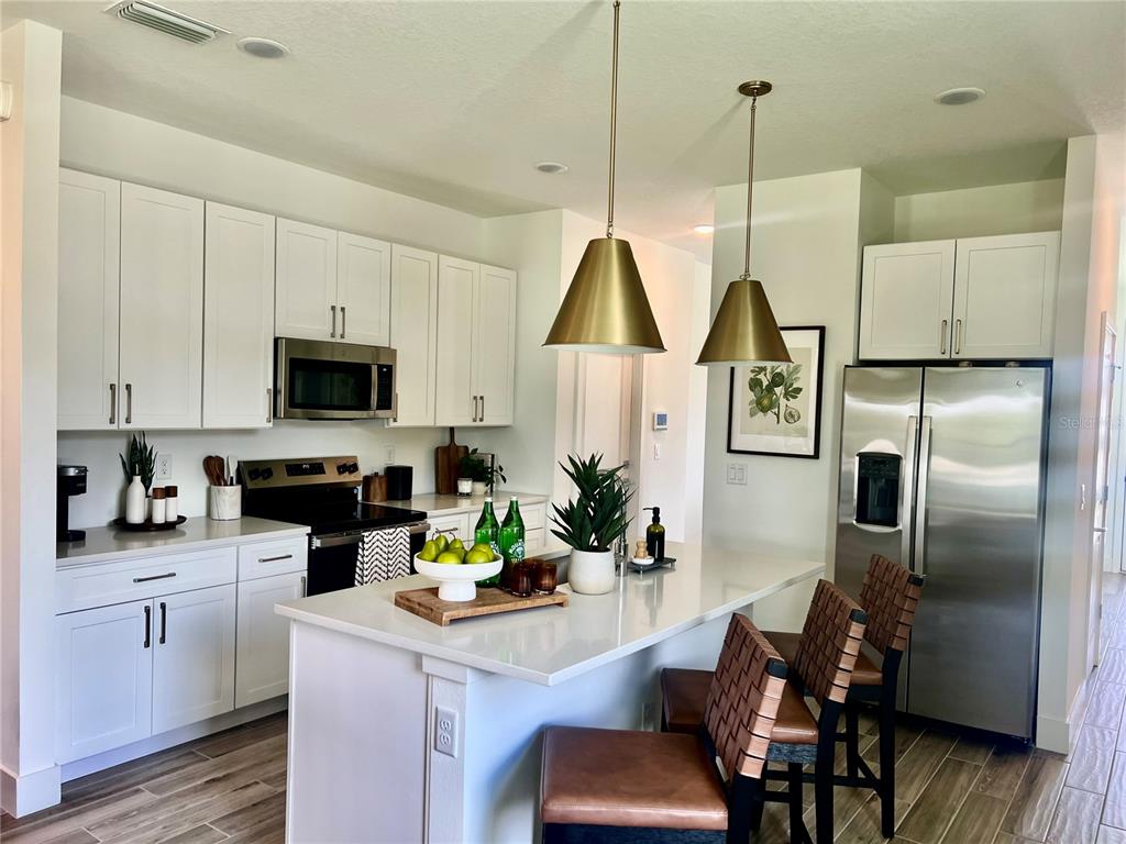 A modern kitchen features white cabinetry, stainless steel appliances, a quartz island, and pendant lighting — 280 ELENA LAVIN CIRCLE, ORLANDO, FL