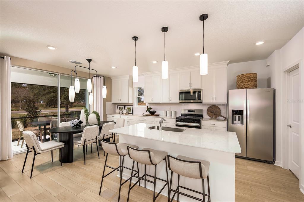 A modern kitchen features a white island with bar stools, stainless appliances, and dining area — 1420 HAMILTON WAY, LAKE ALFRED, FL