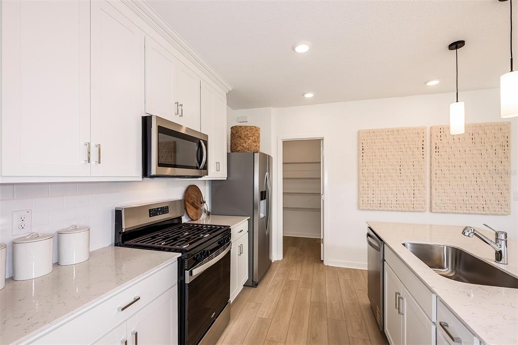 A modern kitchen features white cabinets, stainless steel appliances, quartz countertops, and light wood flooring — 1420 HAMILTON WAY, LAKE ALFRED, FL