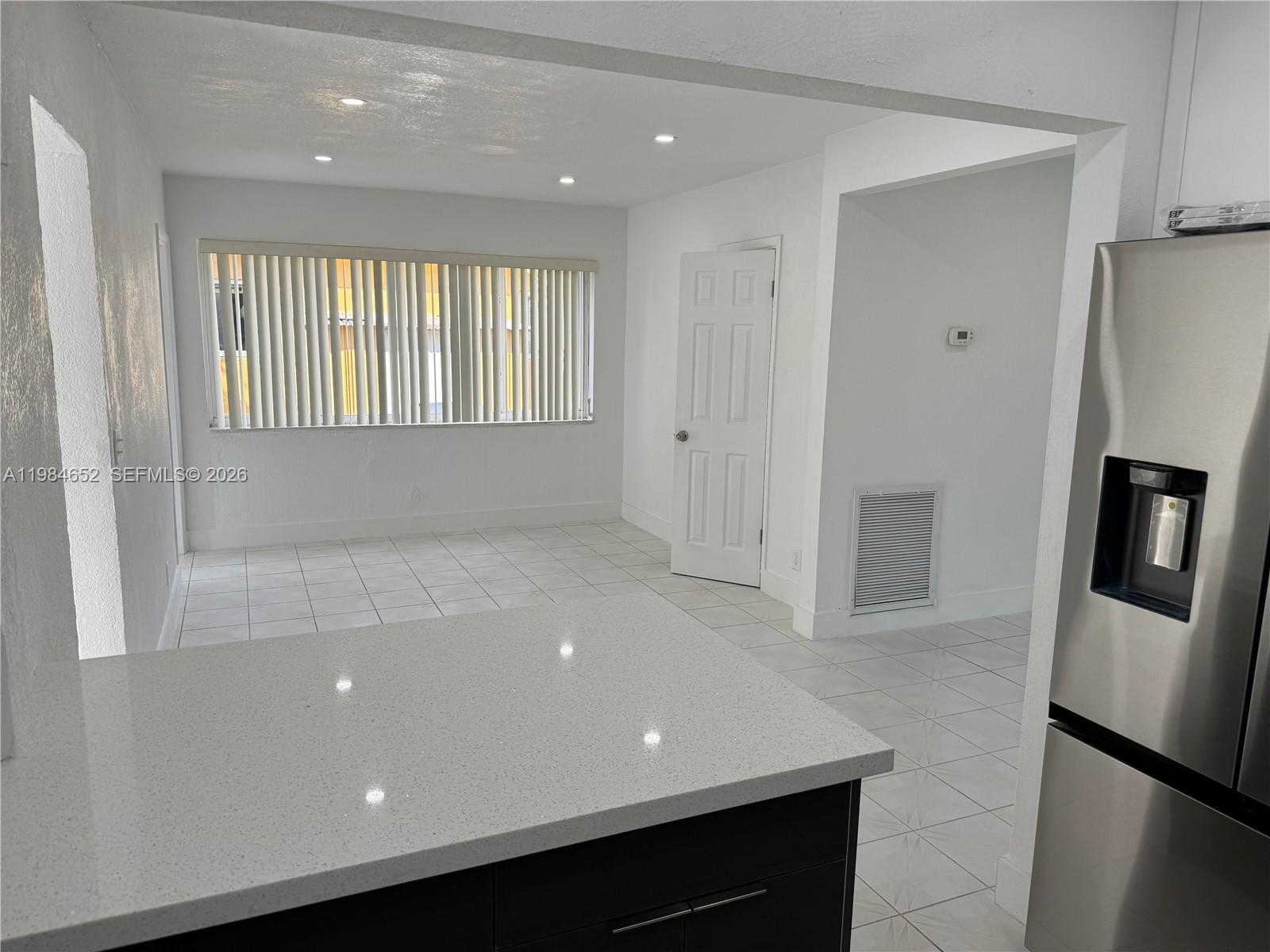 A kitchen island with a quartz countertop overlooks a tiled dining area with vertical blinds — 2400 N 57th Way, Hollywood FL 33021, HOLLYWOOD, FL