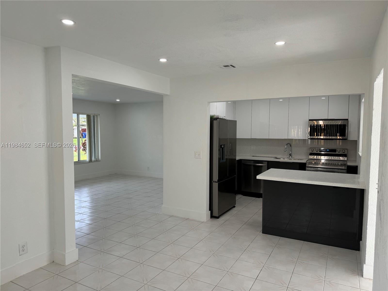 A kitchen with white upper cabinets and a black island opens into a tiled room — 2400 N 57th Way, Hollywood FL 33021, HOLLYWOOD, FL
