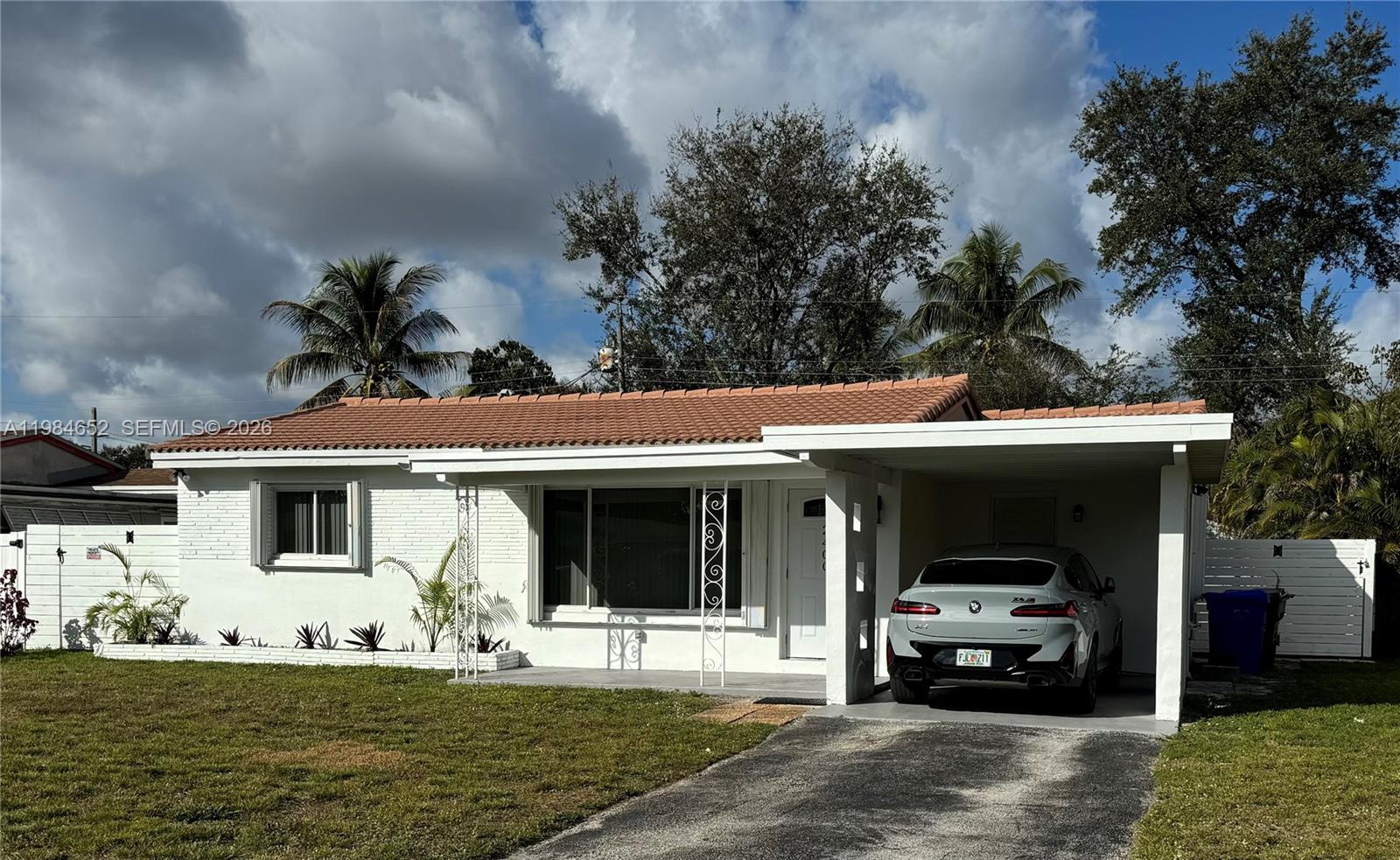 A single-story white house with a tiled roof and a carport featuring a parked car — 2400 N 57th Way, Hollywood FL 33021, HOLLYWOOD, FL