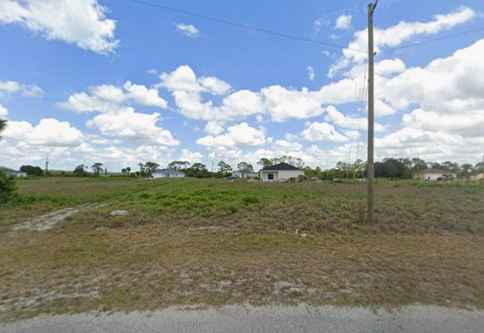 A vacant, grassy lot with a utility pole and distant houses under a cloudy sky — 9050 Green Circle, FL 33935, FL