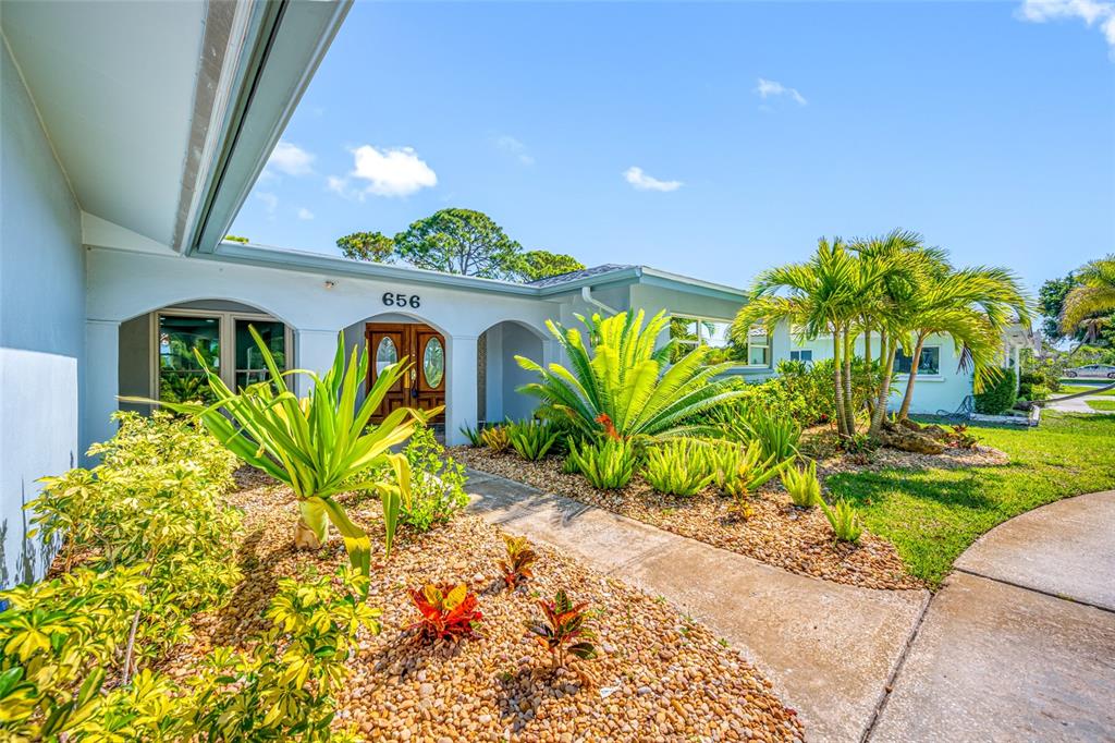 The exterior of a single-story house features a covered entryway, arched columns, and landscaped gardens — 656 MEHLENBACHER ROAD, BELLEAIR, FL