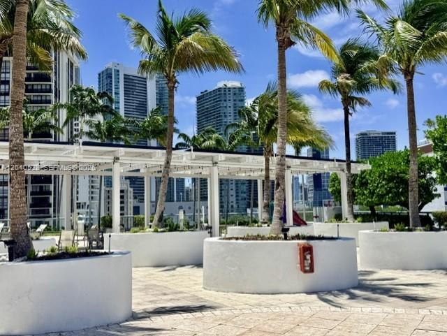 An outdoor patio area features white planters, palm trees, and a pergola against city buildings — 601 NE 36th St # 803, Miami FL 33137, MIAMI, FL