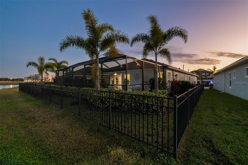 A fenced backyard features a screened-in patio with palm trees at sunset — 5424 SILVER SUN DRIVE, APOLLO BEACH, FL