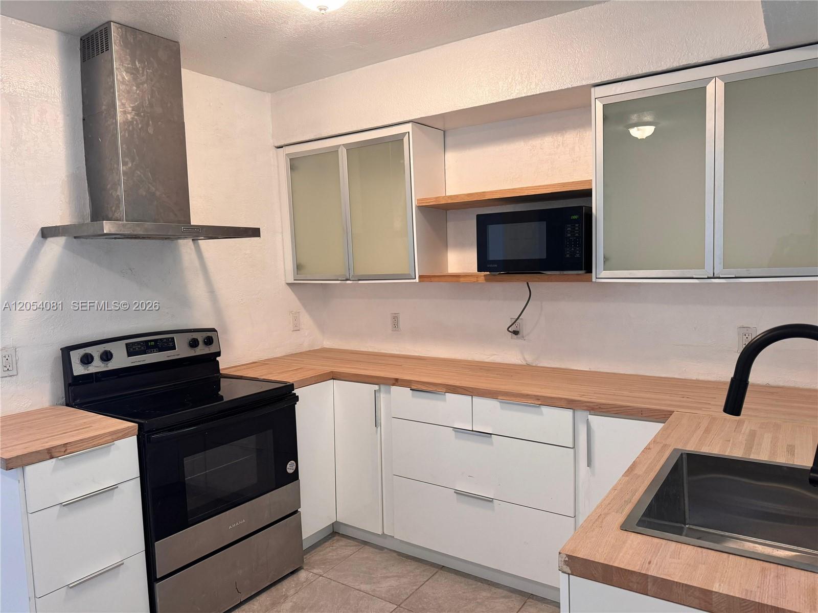 A kitchen features white cabinets, wood countertops, a stainless steel range, and a range hood — 146 NW 56th St # 146, Miami FL 33127, MIAMI, FL