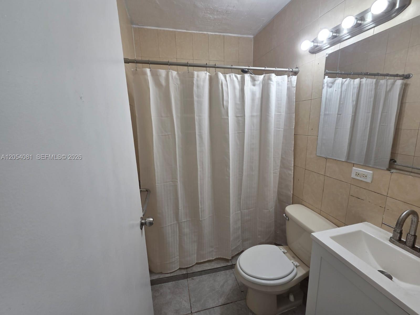 A bathroom features a shower with a white curtain, a toilet, and a vanity sink — 146 NW 56th St # 146, Miami FL 33127, MIAMI, FL