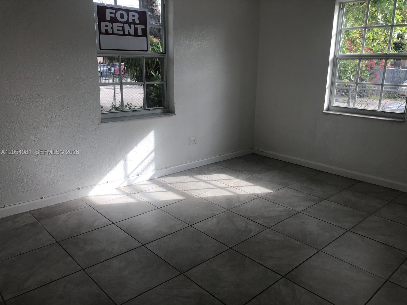 An empty room with white walls, gray tile flooring, and two windows with exterior views — 146 NW 56th St # 146, Miami FL 33127, MIAMI, FL