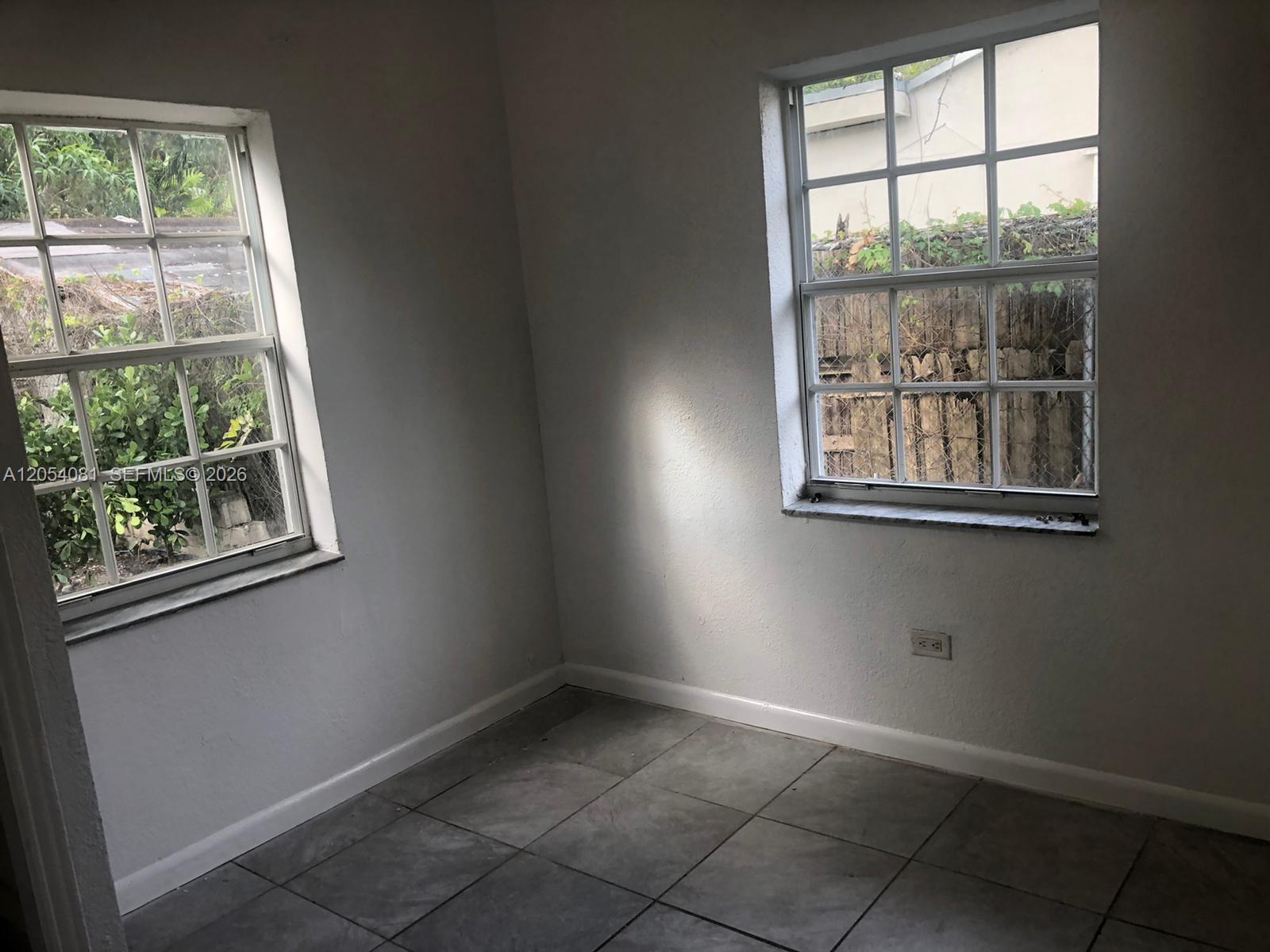 An empty room features gray tile flooring, white walls, and two windows with exterior views — 146 NW 56th St # 146, Miami FL 33127, MIAMI, FL