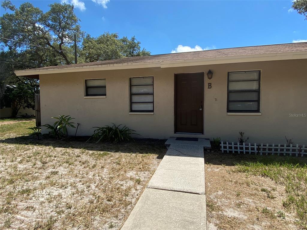 The exterior of a single-story tan house features a brown front door labeled B — 301 WOODROW AVENUE UNIT B, LARGO, FL