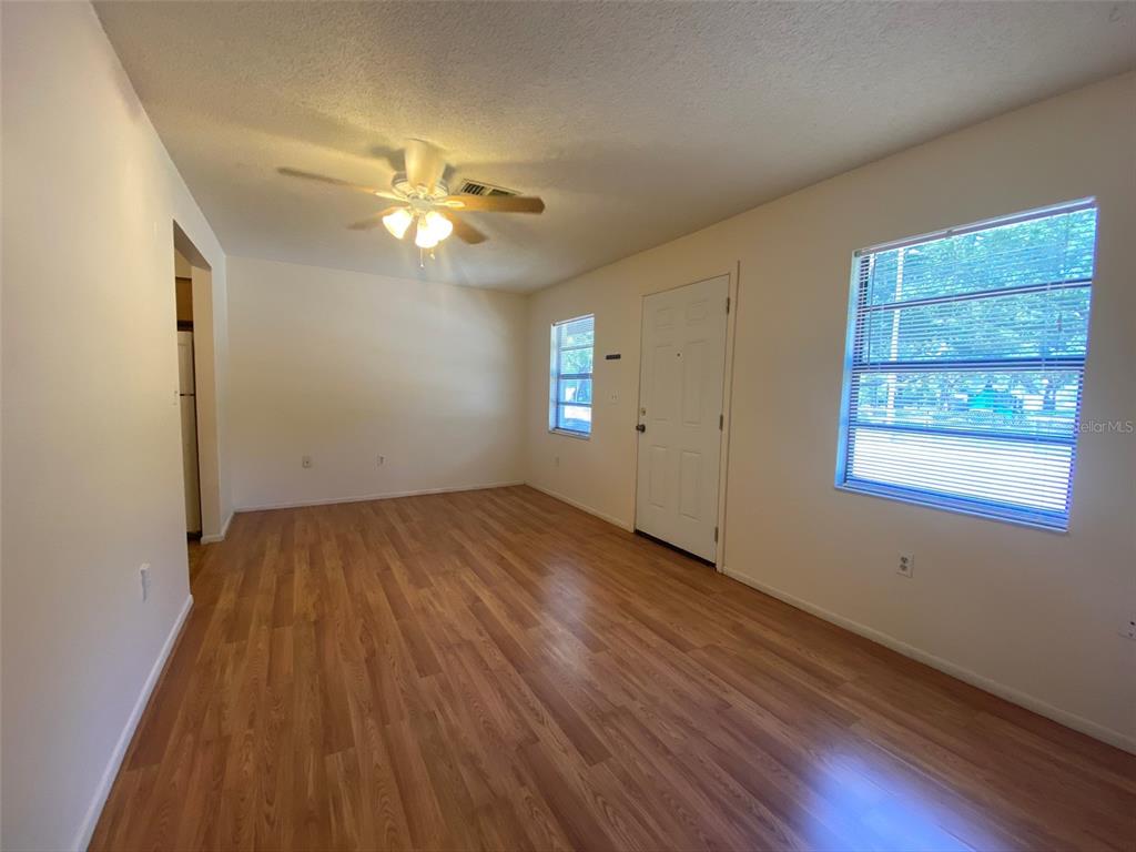 An empty living room features wood-look flooring, a ceiling fan, and a white entry door — 301 WOODROW AVENUE UNIT B, LARGO, FL