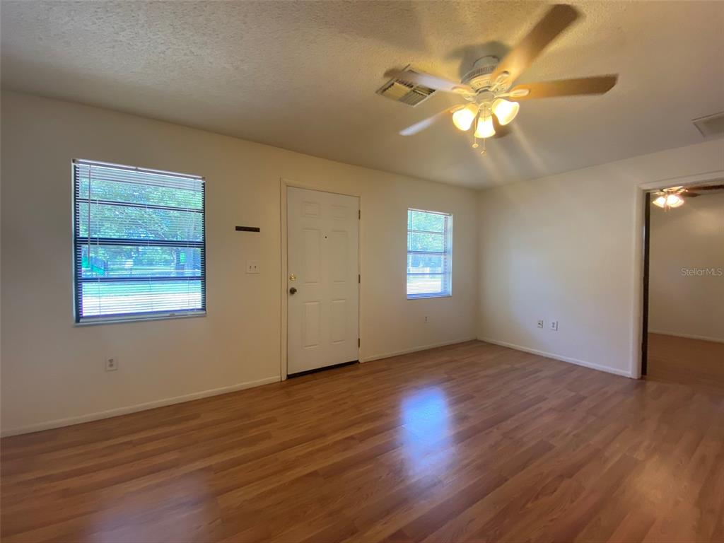An empty living room features light wood-look flooring, white walls, a ceiling fan, and windows — 301 WOODROW AVENUE UNIT B, LARGO, FL