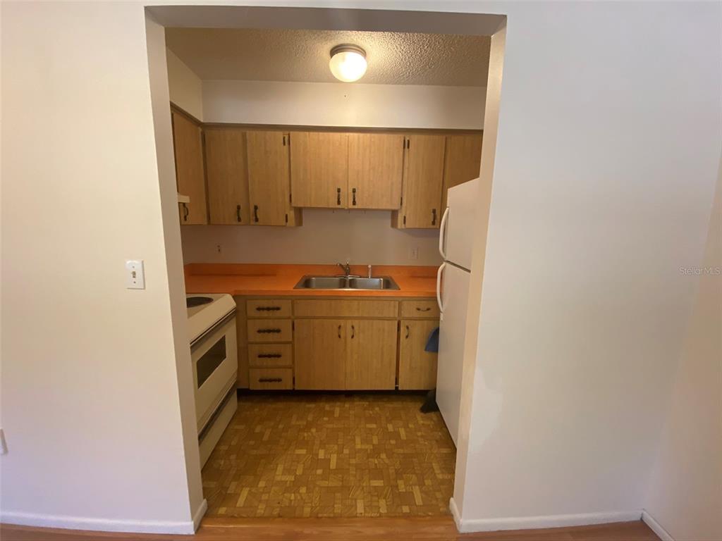 A galley kitchen features light wood cabinets, orange laminate countertops, and a white refrigerator — 301 WOODROW AVENUE UNIT B, LARGO, FL