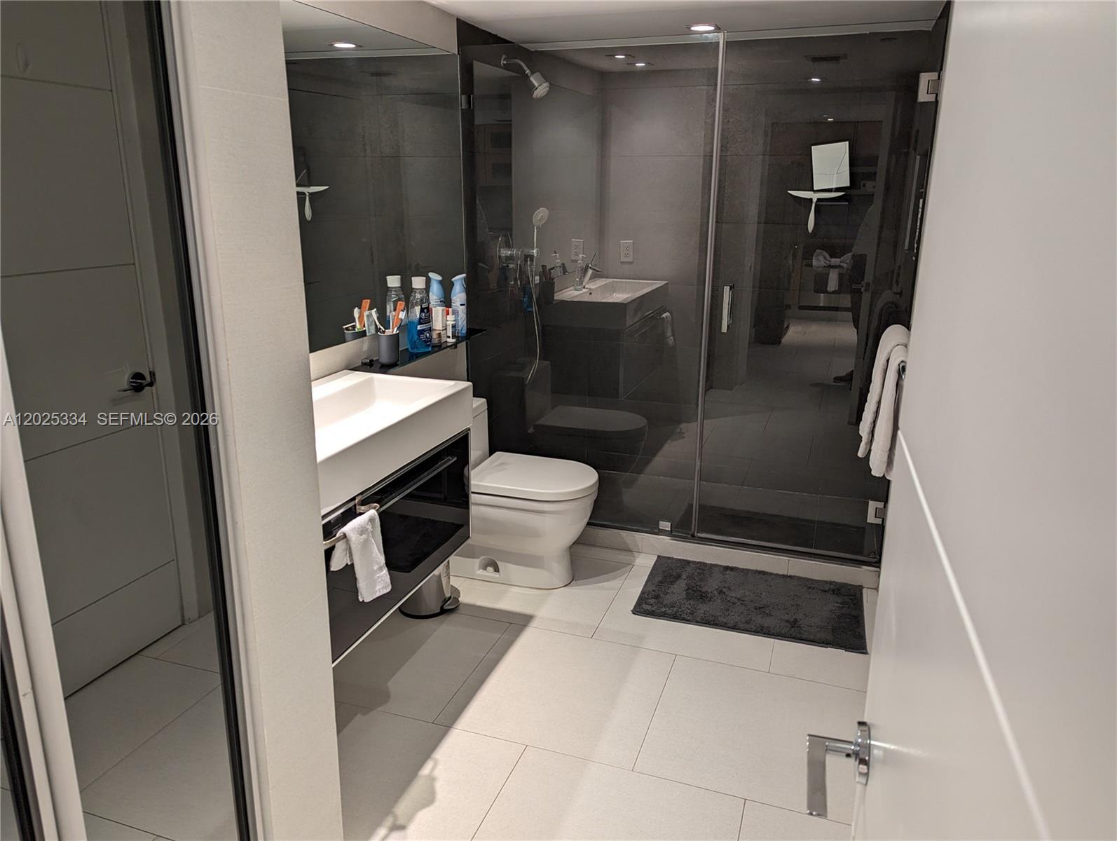 A modern bathroom features a floating vanity, a glass-enclosed shower, and light-colored floor tiles — 2101 Brickell Ave # 1104, Miami FL 33129, MIAMI, FL