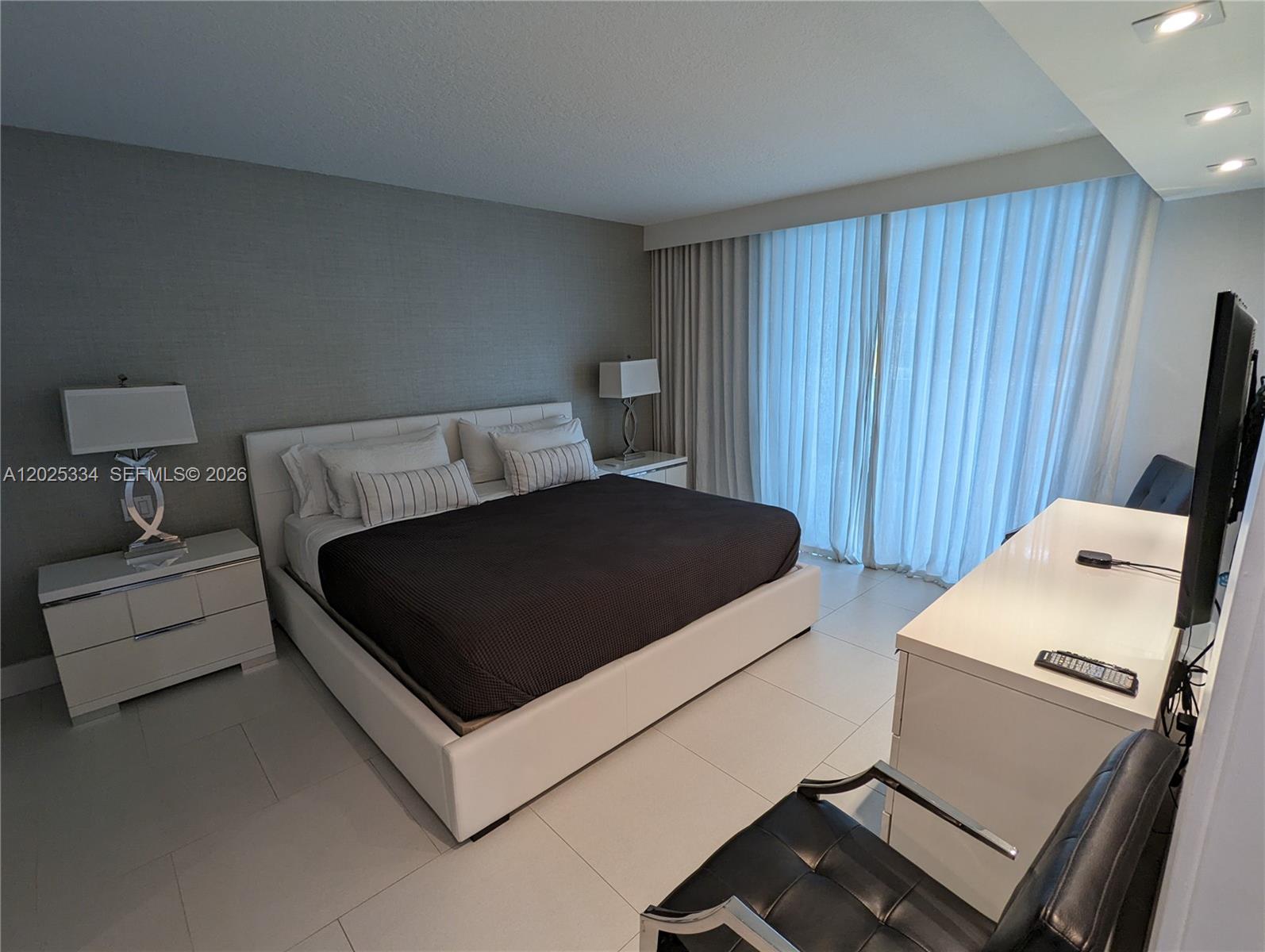 A modern bedroom features a white bed, matching nightstands, and a desk with a chair — 2101 Brickell Ave # 1104, Miami FL 33129, MIAMI, FL