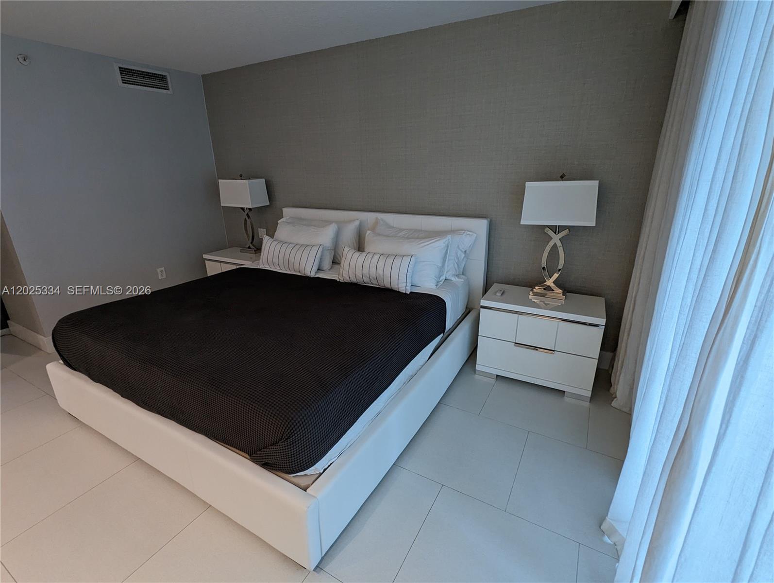 A bedroom features a white bed frame, dark bedding, and two white nightstands with lamps — 2101 Brickell Ave # 1104, Miami FL 33129, MIAMI, FL