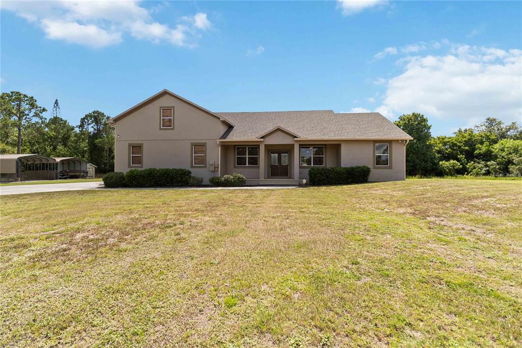 A tan, two-story house with a gabled roof sits on a large, grassy lot — 1300 S NARCOOSSEE ROAD, ST CLOUD, FL