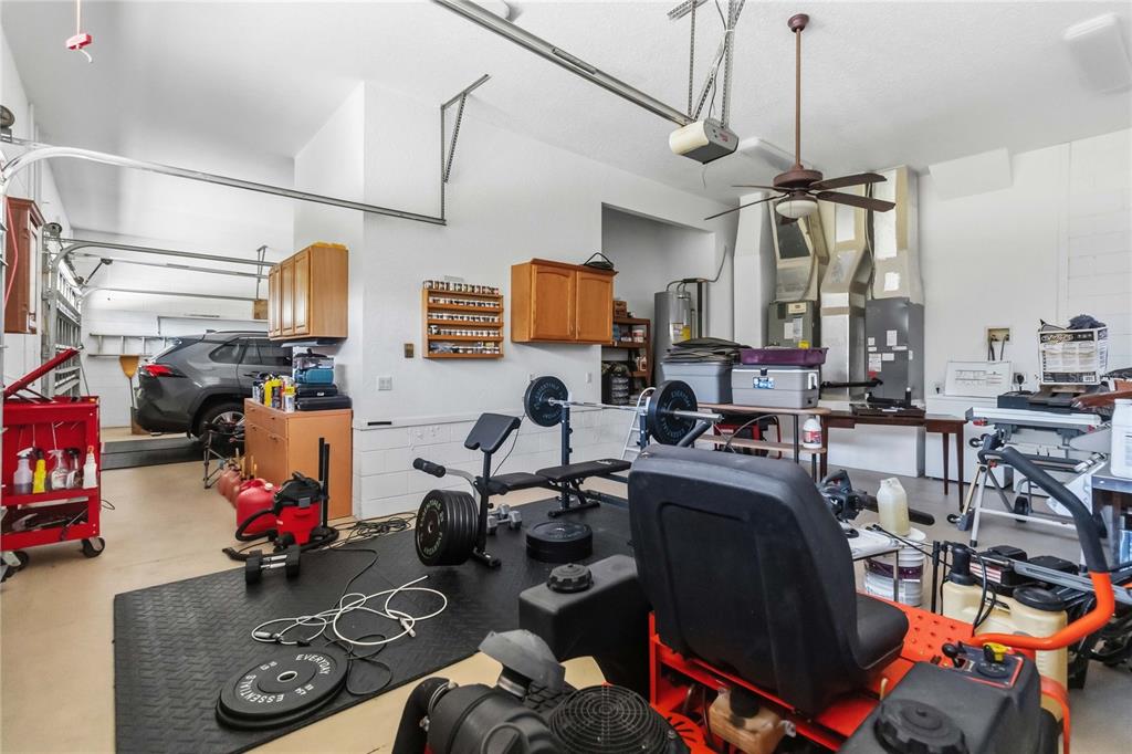 A garage with a home gym area, storage cabinets, a vehicle, and a riding lawnmower — 1300 S NARCOOSSEE ROAD, ST CLOUD, FL