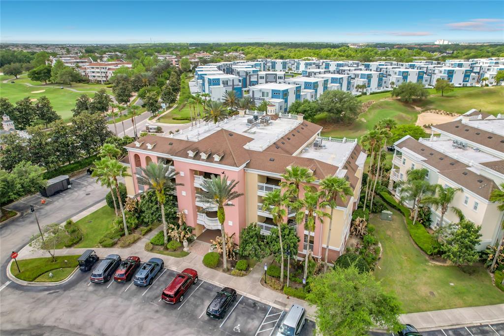 An aerial view shows a multi-story apartment building with a pink facade and parking lot — 1116 SUNSET VIEW CIRCLE UNIT 304, REUNION, FL