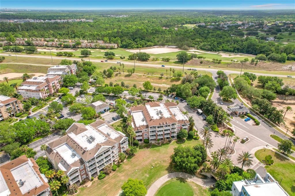 An aerial view shows multi-story apartment buildings surrounded by lush landscaping, parking lots, and a golf course — 1116 SUNSET VIEW CIRCLE UNIT 304, REUNION, FL