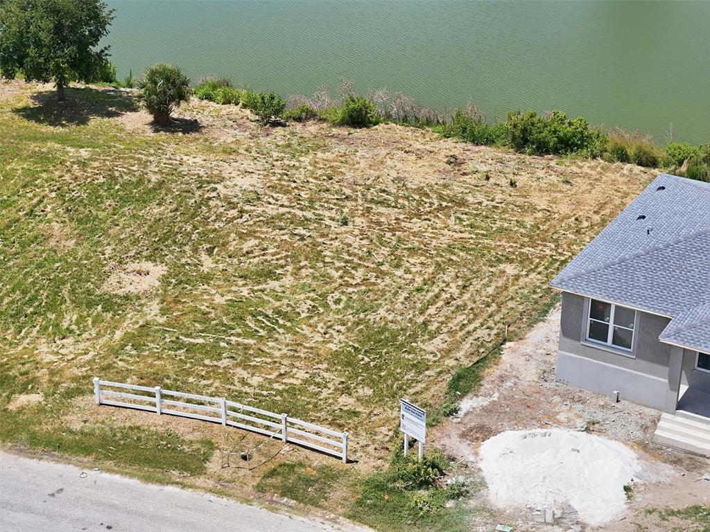 An aerial view shows a vacant residential lot next to a house near a lake — 1504 JACKSON DRIVE, HOLIDAY, FL