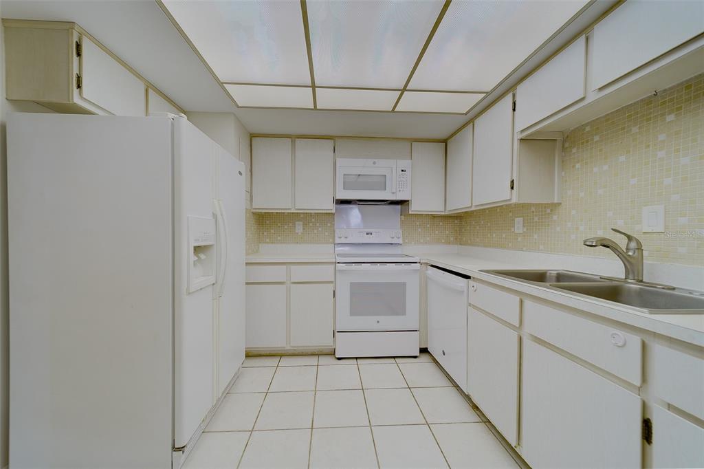 A galley kitchen features white appliances, white cabinetry, a tiled backsplash, and a drop ceiling — 17920 GULF BOULEVARD UNIT 1408, REDINGTON SHORES, FL