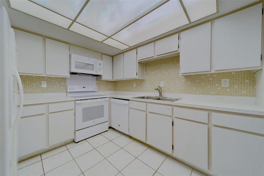A kitchen with white cabinets, white appliances, a tiled backsplash, and a drop ceiling — 17920 GULF BOULEVARD UNIT 1408, REDINGTON SHORES, FL